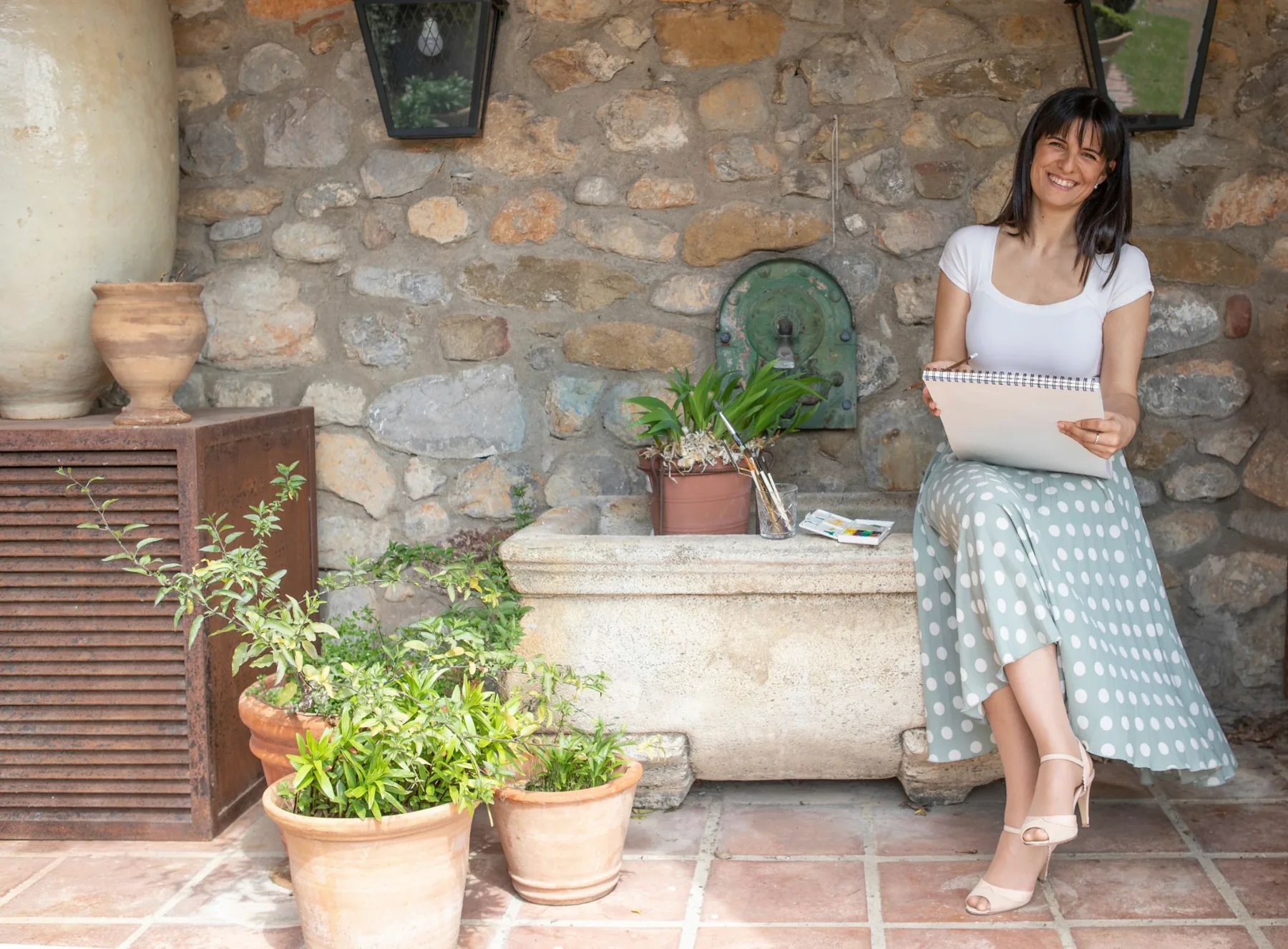 Elisabet con un cuaderno de dibujo junto a una fuente de piedra
