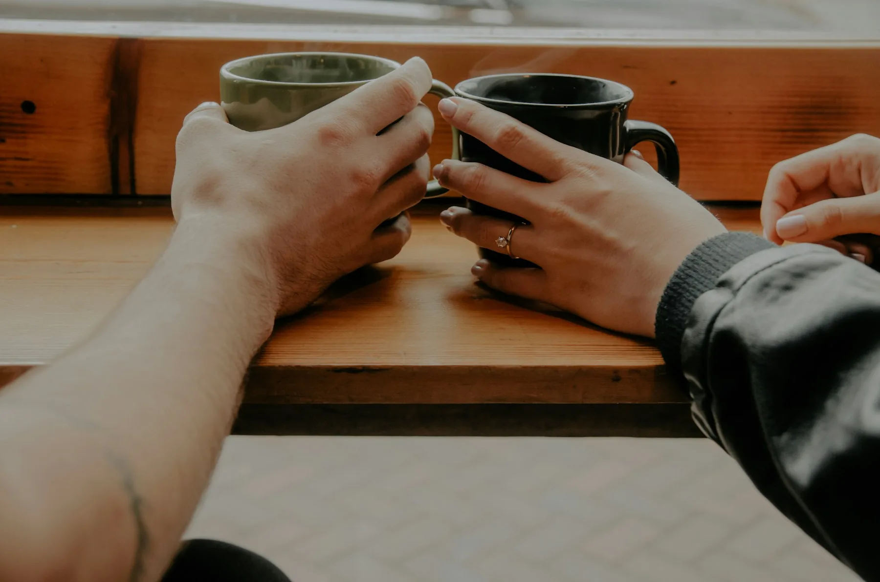 Dos personas sentadas una junto a la otra, cada una con su taza, frente a una barra de madera